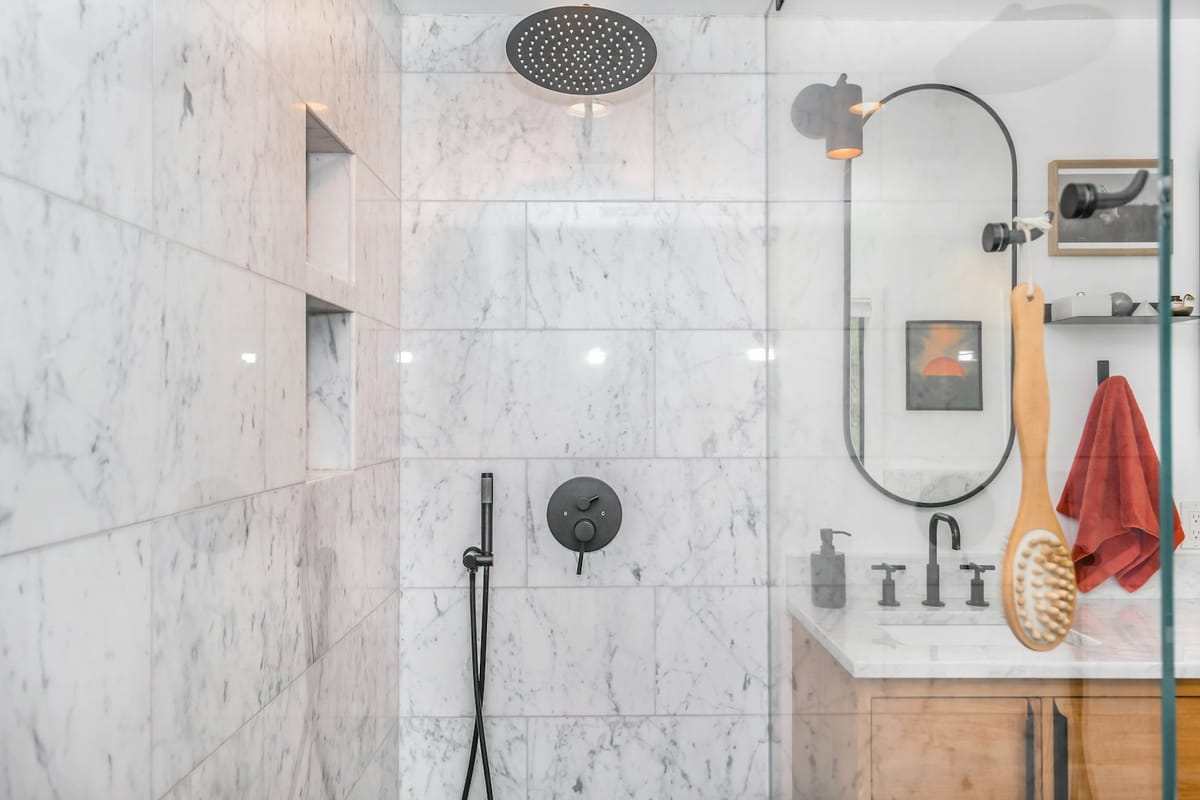 Ny bruseniche med marmorfliser, sort armatur og glasvæg efter renovering