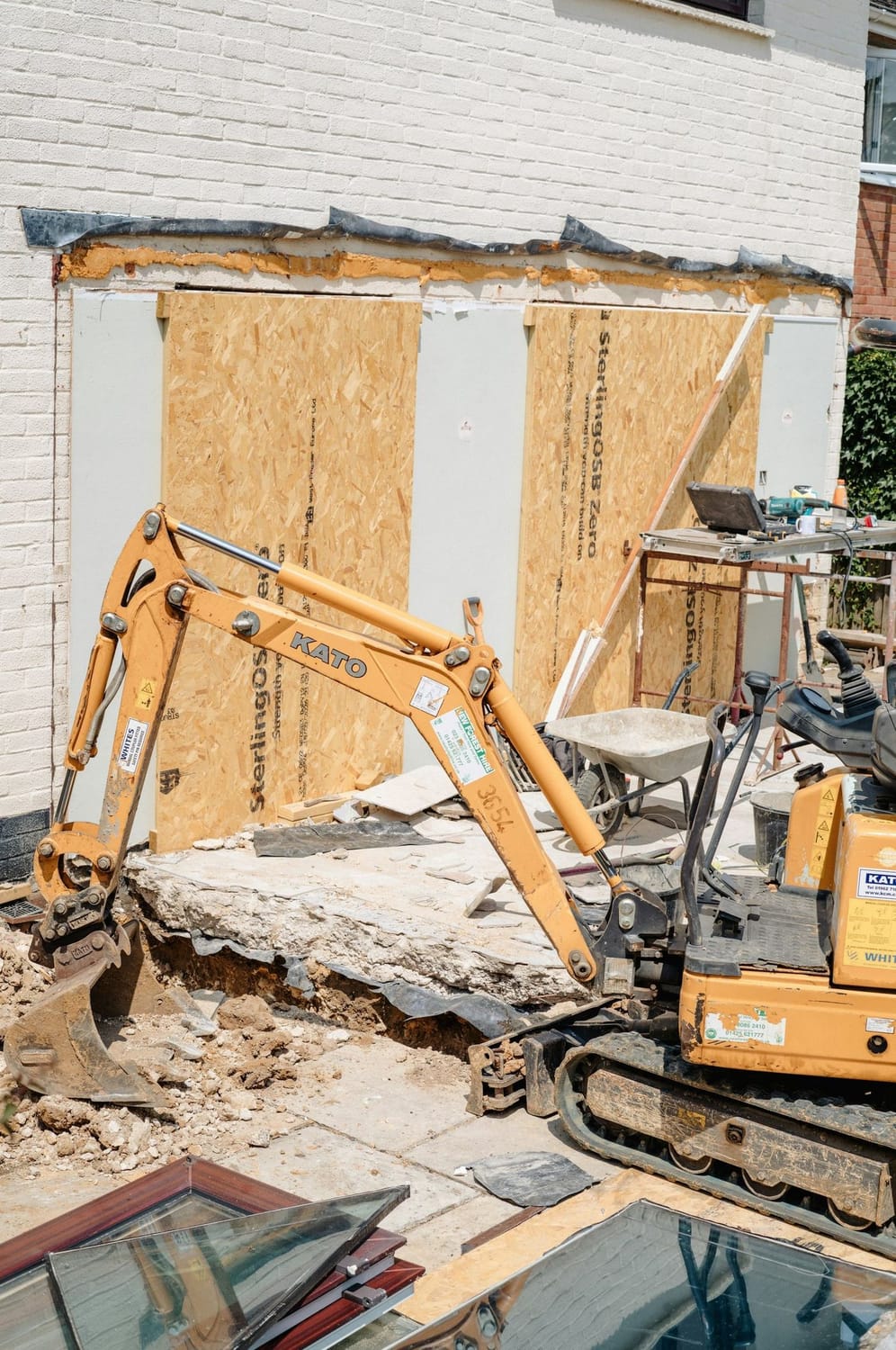 Minigraver bryder terrassen op ved en husgavl under ombygning