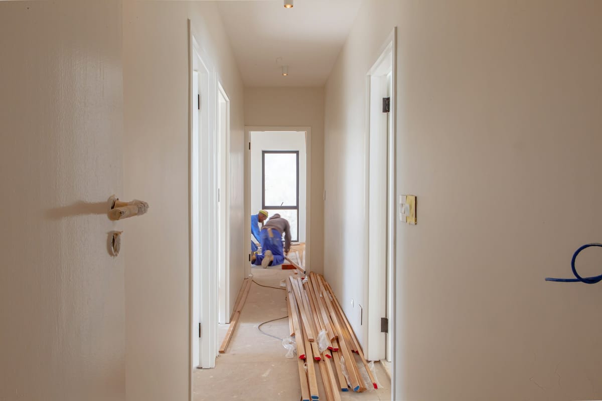Nypudset gang i hus under renovering med gulvlister klar på gulvet og håndværkere i baggrunden