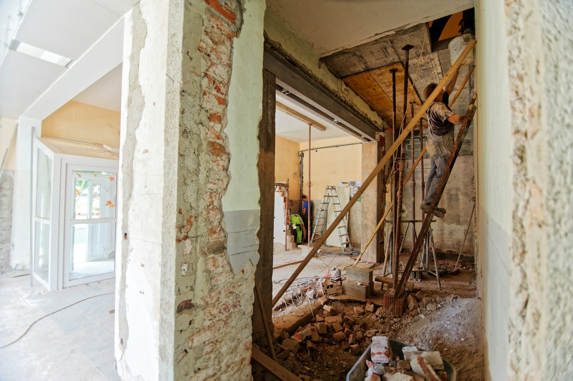 Hus under totalrenovering med afdækkede vægge, stålbjælke over en ny åbning og håndværker på stige