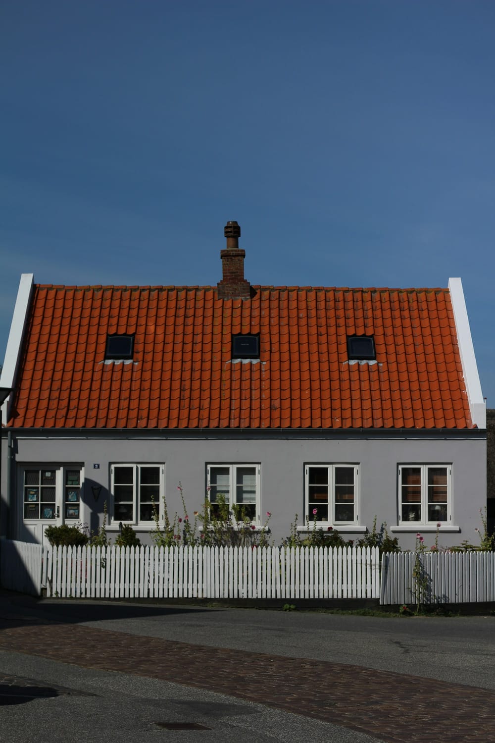 Gråt hus med rødt tegltag bag et hvidt stakit